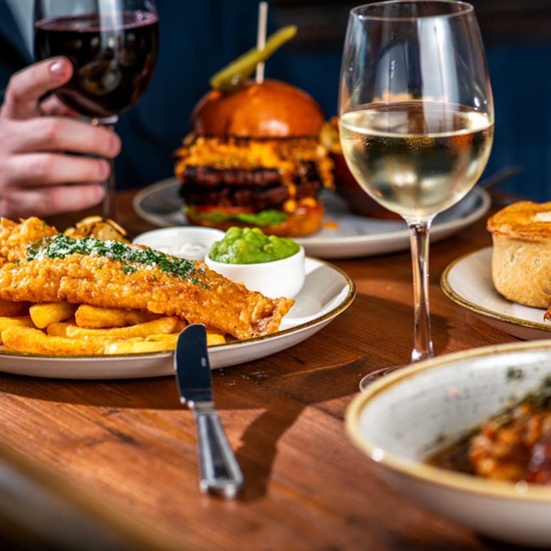 The Scarbrough Hotel — golden fish and chips with wine glasses and a stacked burger on a pub table