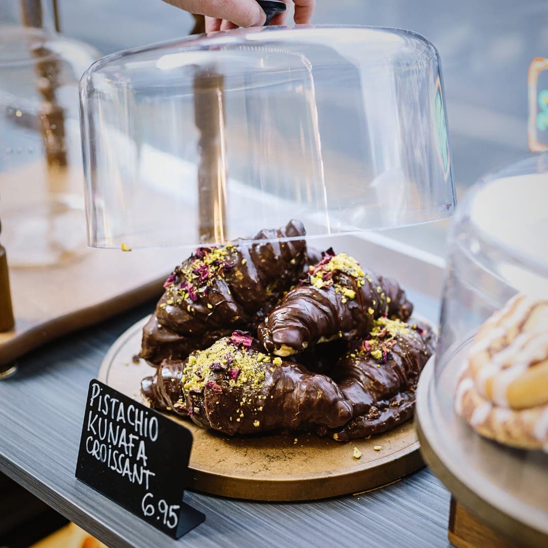 Pistachio kunafa croissants topped with rose petals under a glass dome at Caffeine Addict
