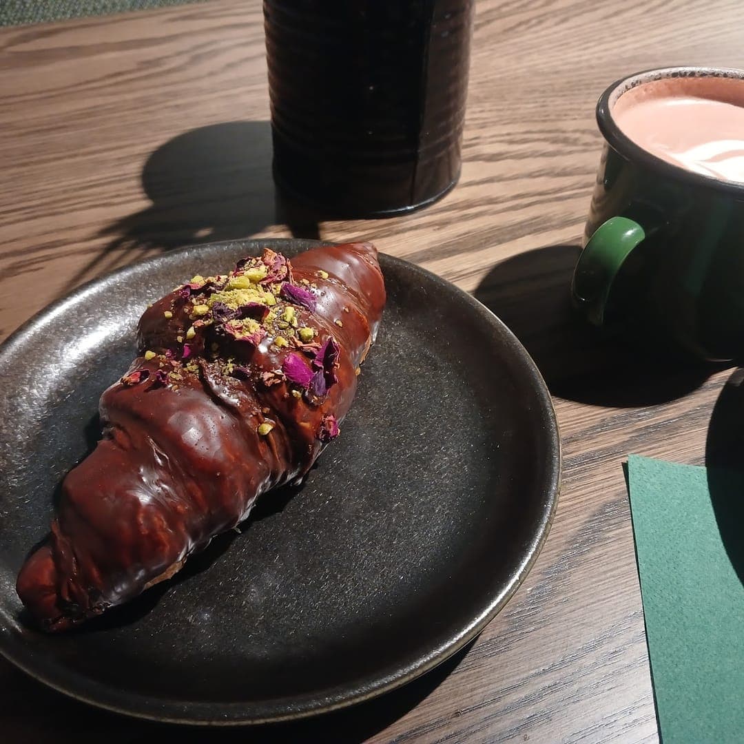 Chocolate croissant topped with rose petals and pistachio served with a hot drink at Caffeine Addict