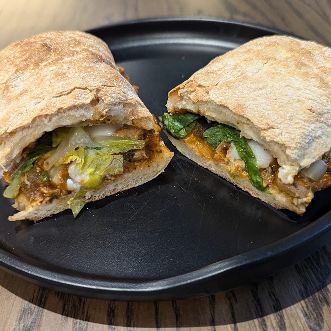 Stuffed ciabatta sandwich cut in half on a dark plate at Caffeine Addict Headingley