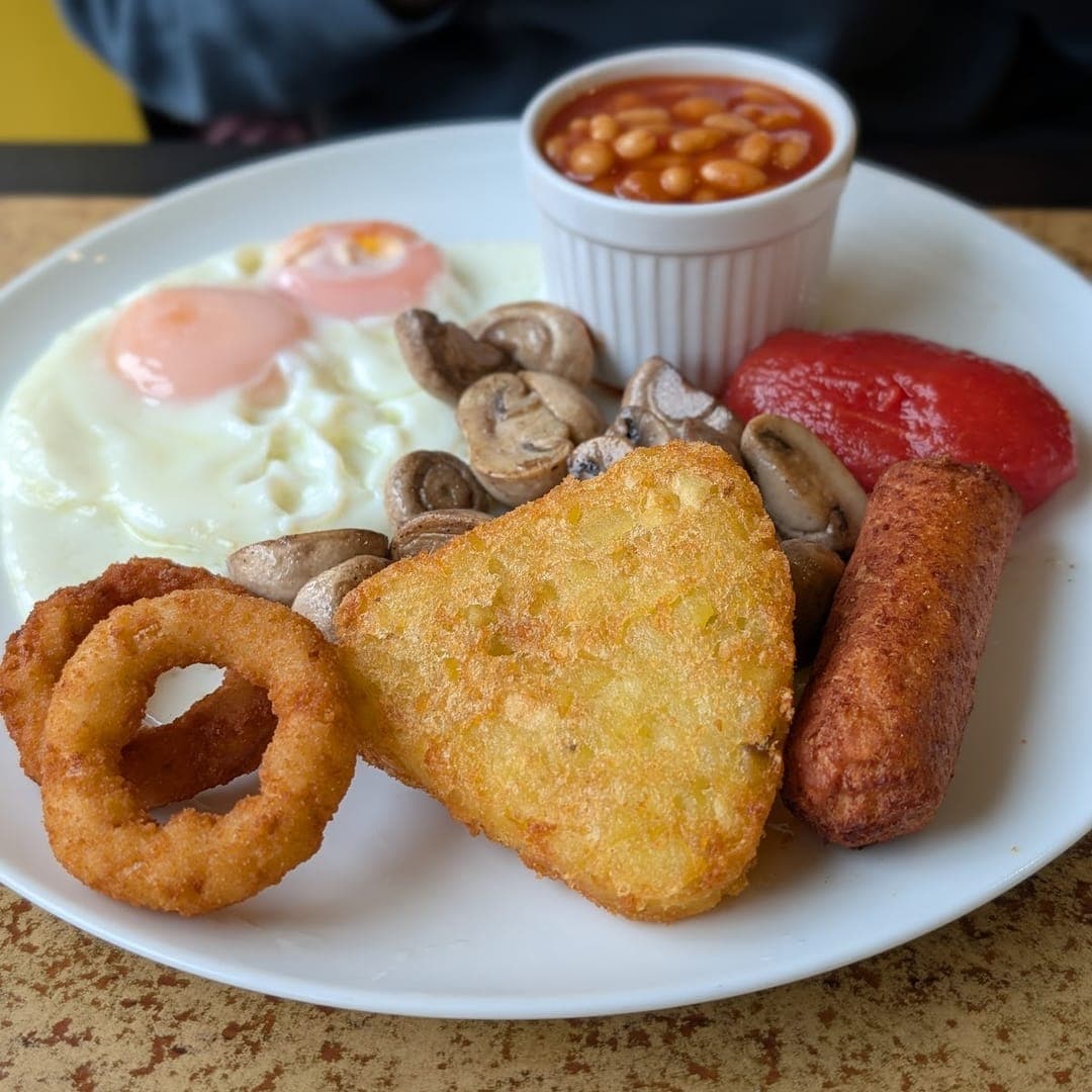 Full English breakfast with hash browns, beans, sausage, egg, and onion ring at Chichini