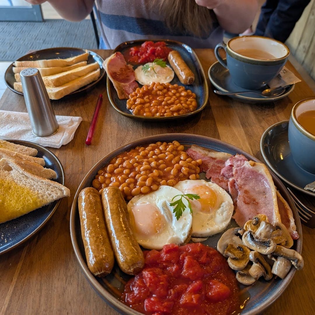 Full English breakfast spread with eggs, sausages, beans, bacon, and tea at Country Crust