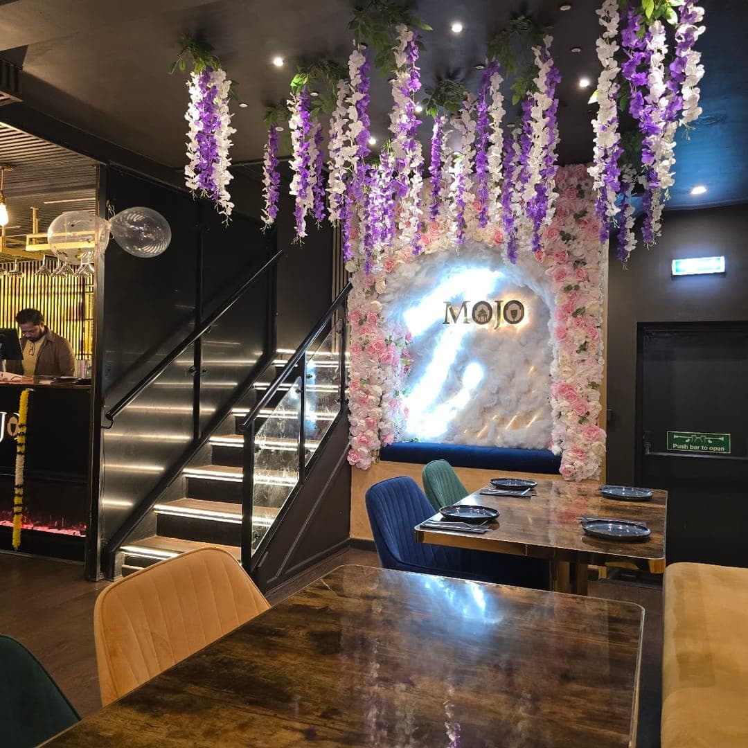 Entrance of Mojo Royal Treat with hanging flower installation, MOJO sign, and staircase