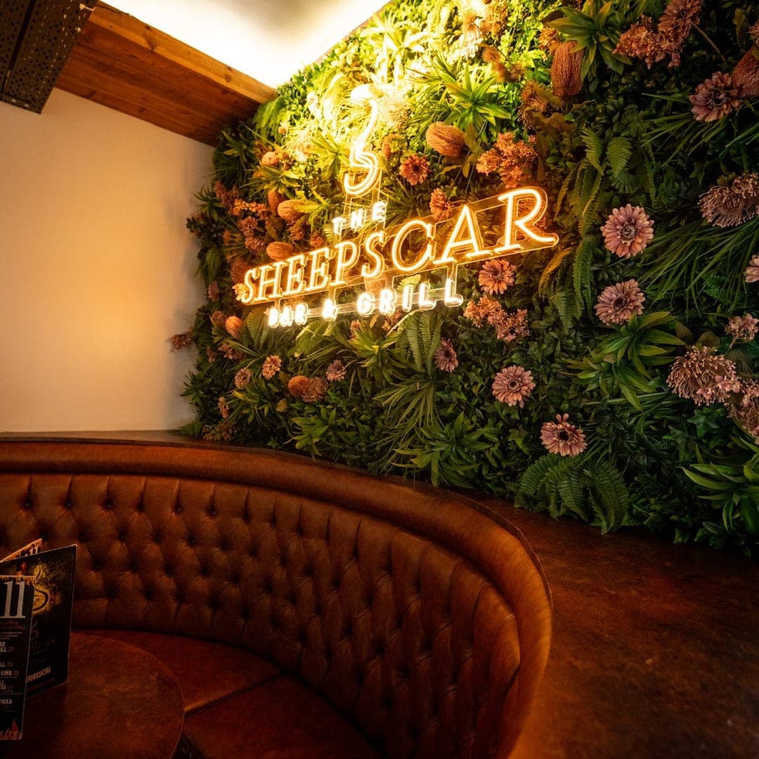 Flower wall with neon Sheepscar Bar and Grill sign and leather booth seating