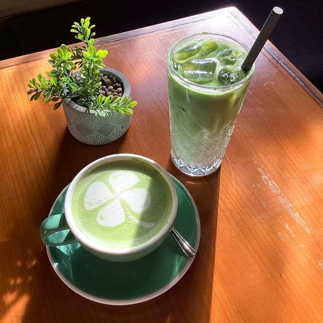 Grounded & Co — hot matcha latte with clover latte art and iced matcha on a wooden table
