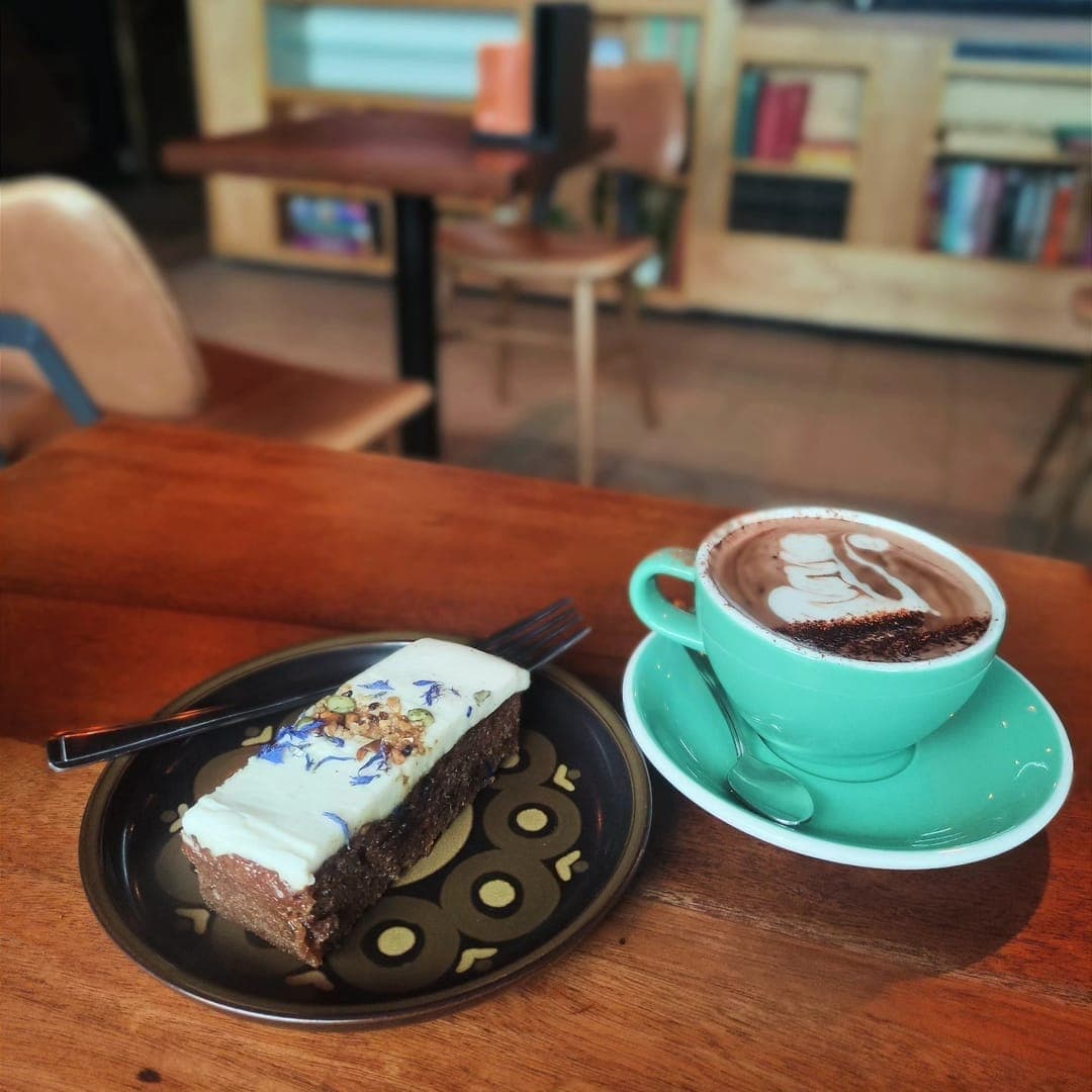 Grounded & Co — carrot cake slice and hot chocolate on a wooden table with cafe interior behind