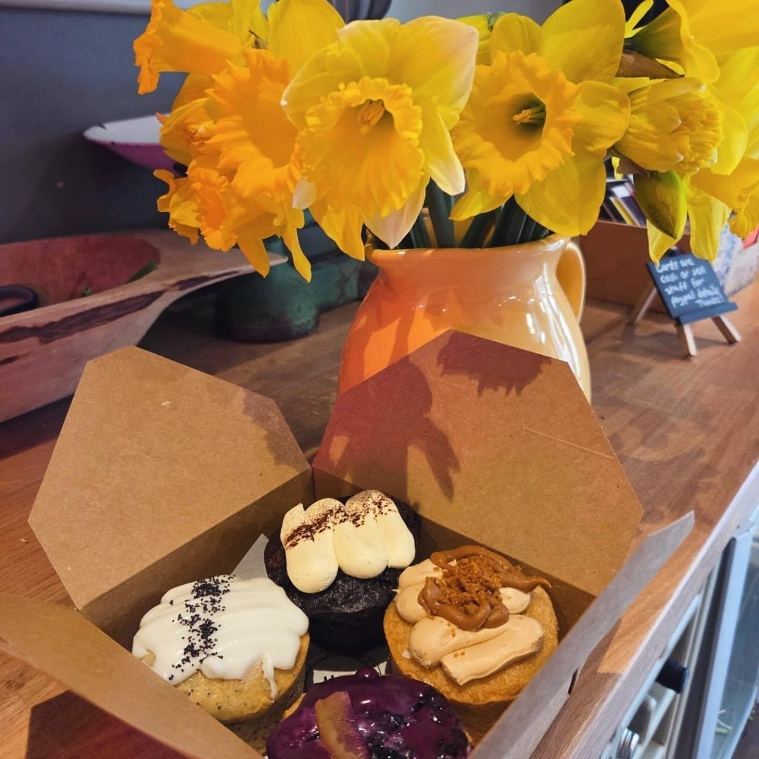 MISTÅL Kitchen — assorted cakes in a takeaway box with yellow daffodils