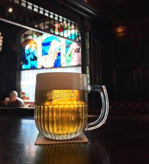 The Bankers Cat Budvar tankard in foreground with stained glass window dramatically lit behind