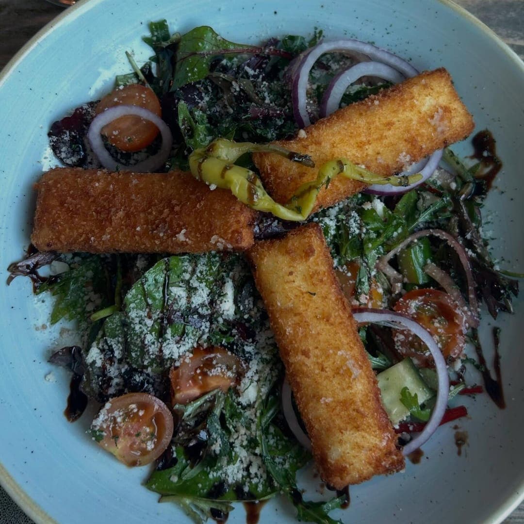 The Good Luck Club — crispy halloumi salad with mixed greens and red onion on a blue ceramic plate