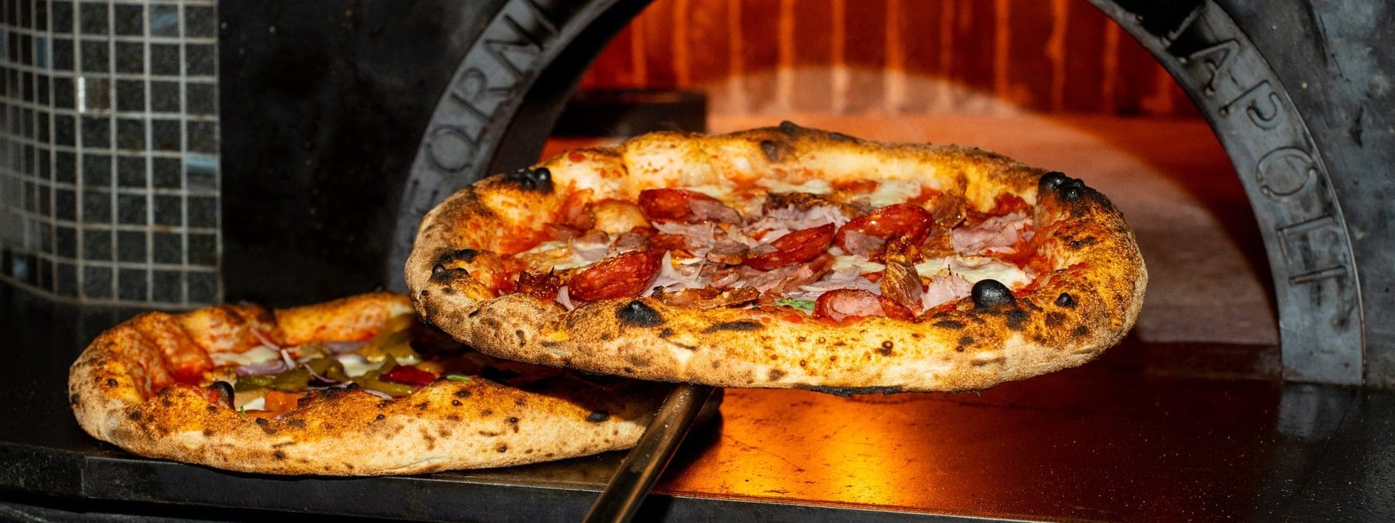 VESUVIUS — two Neapolitan pizzas being pulled from a wood-fired oven