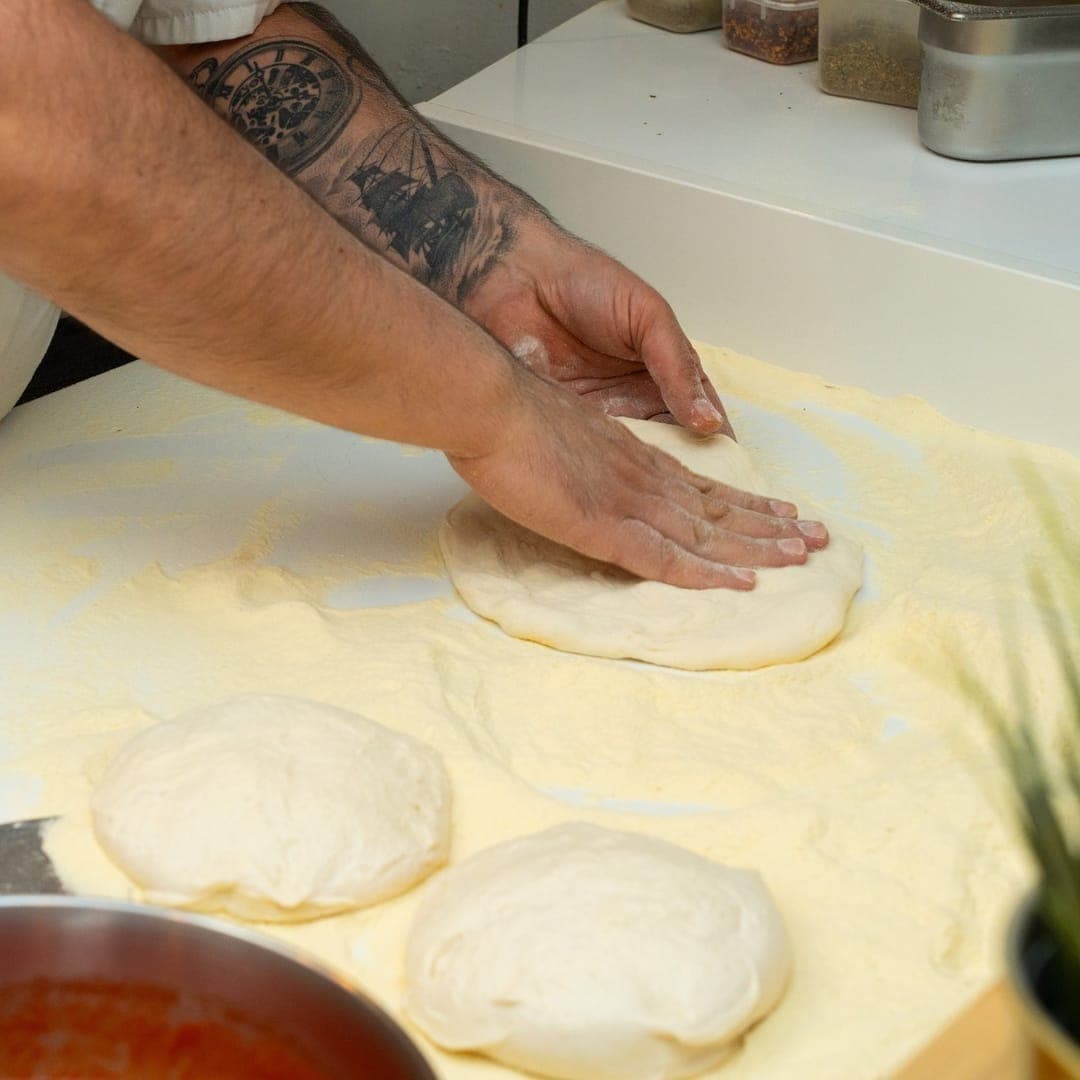 VESUVIUS — tattooed chef hands pressing pizza dough on a floured surface