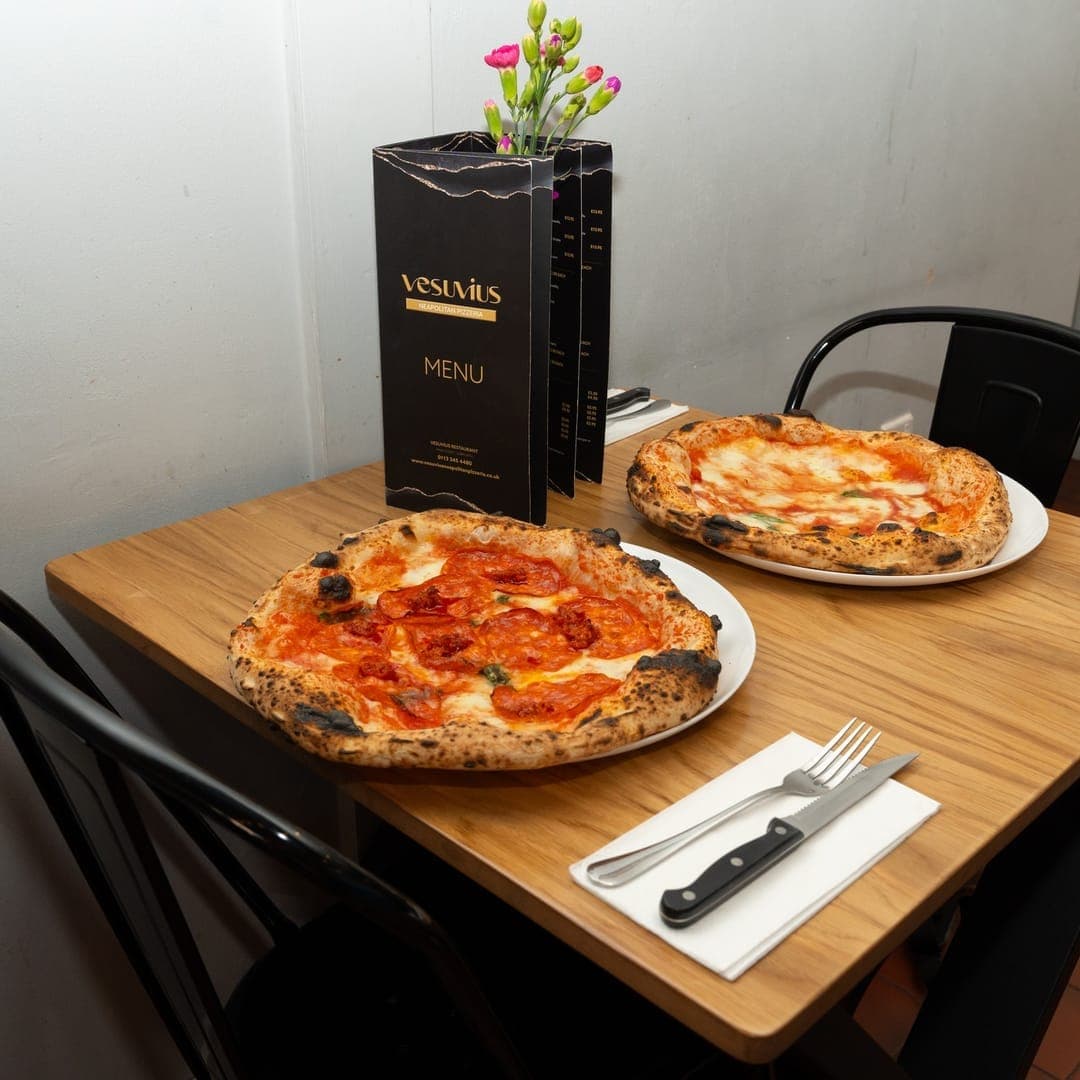 VESUVIUS — two Neapolitan pizzas on a restaurant dining table with menu