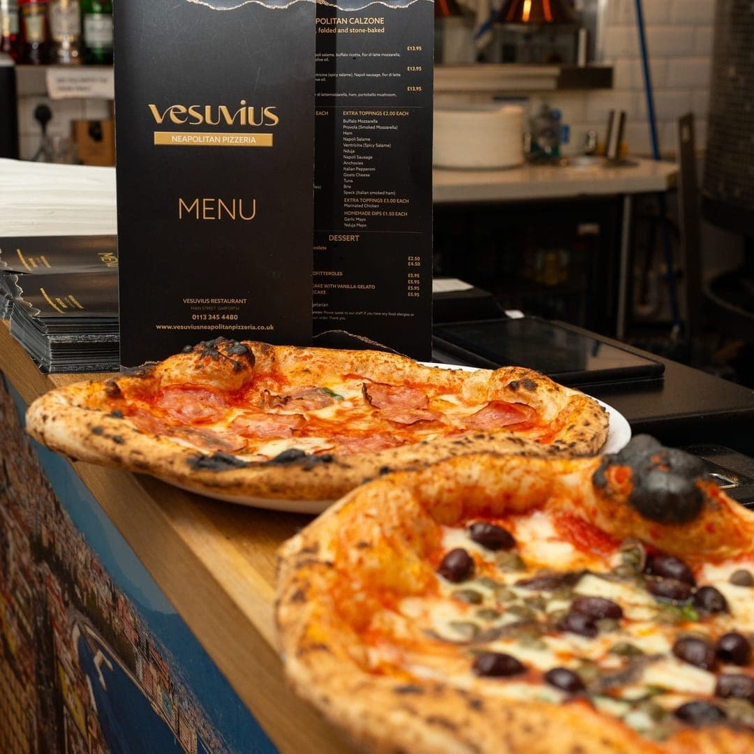 VESUVIUS — two pizzas on the counter in front of the Vesuvius menu board
