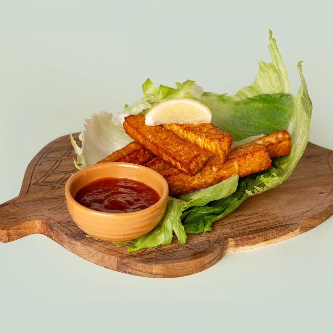 Halloumi fries on a wooden board with salad leaves, lemon and a pot of chilli dipping sauce