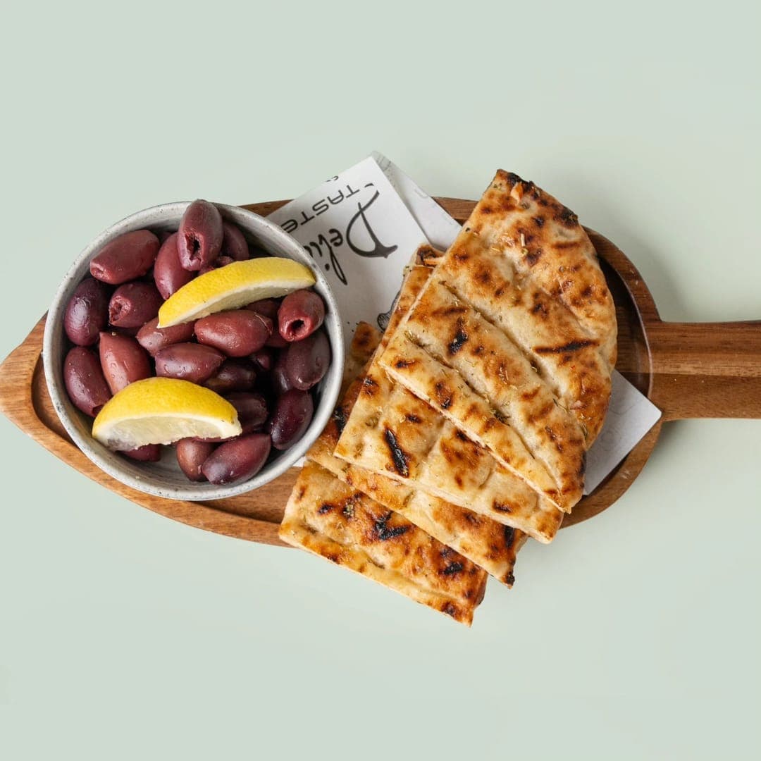 Pitta and olives starter — Kalamata olives with lemon wedges alongside chargrilled pitta bread on a wooden paddle board