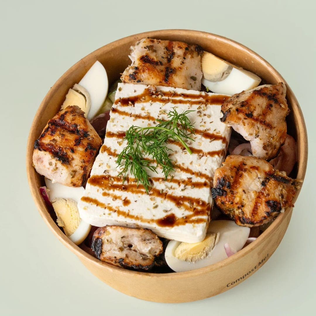 Yiros Salad with grilled chicken pieces, a block of feta, boiled egg, red onion and dill garnish in a compostable bowl