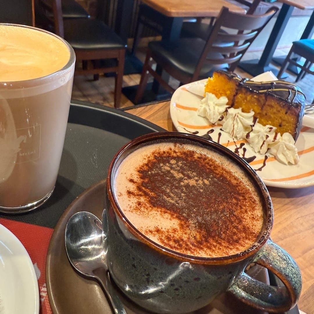 96 location Cafe — cappuccino with cinnamon dusting and a slice of cake