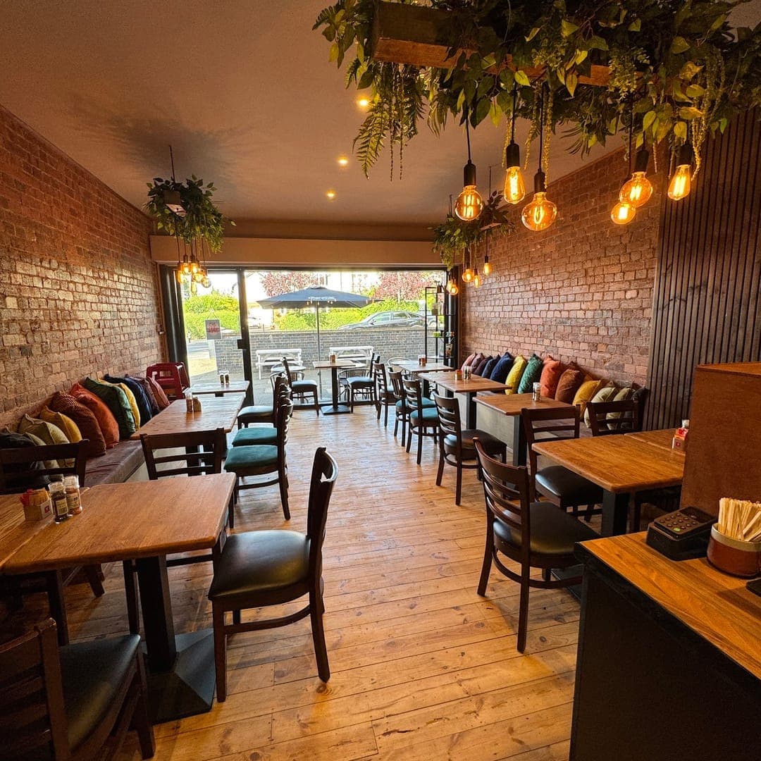96 Location Cafe interior with exposed brick walls, hanging plants, Edison bulb lighting and wooden tables
