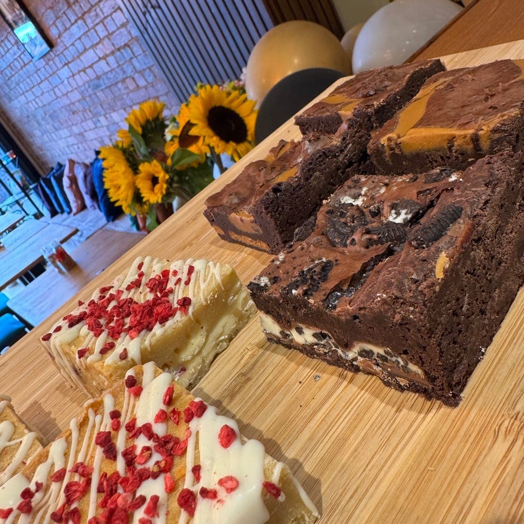 96 Location Cafe brownies and white chocolate traybake displayed on a wooden board with sunflowers in background