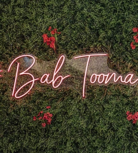 Bab Tooma Leeds — pink neon sign on lush green plant wall with red flowers