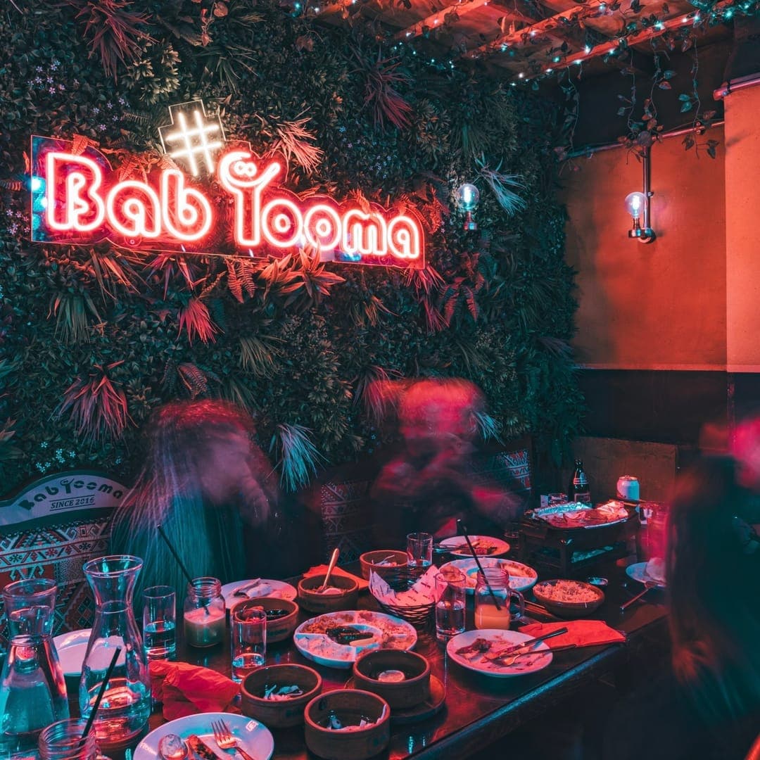 Bab Tooma Leeds — diners beneath the neon Bab Tooma sign on a lush green plant wall