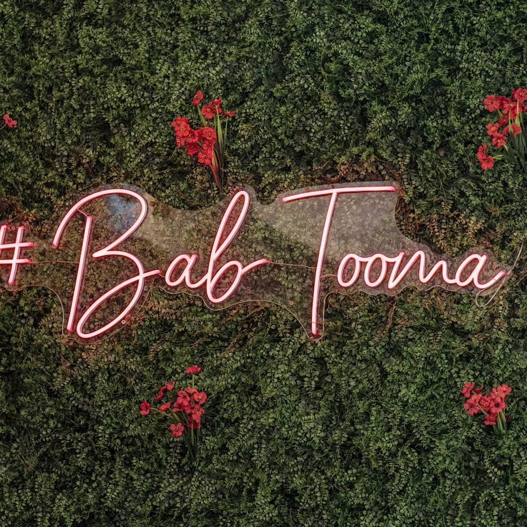 Bab Tooma Leeds — pink neon hashtag sign on green botanical wall with red flowers