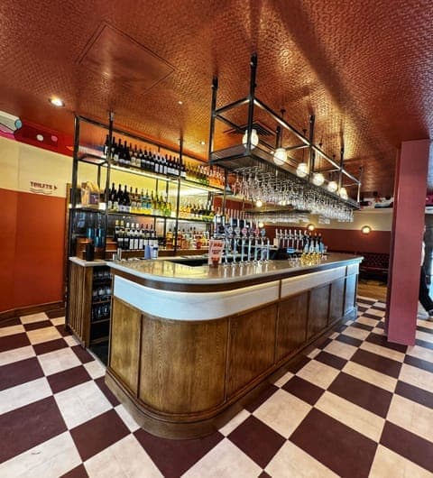 The bar at Brewery Wharf Tavern with a curved wooden counter, checkerboard floor, copper ceiling and rows of beer taps