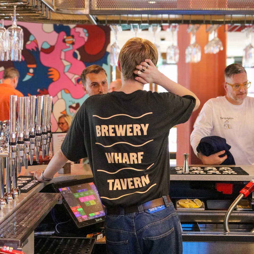 Bartender at work behind the bar at Brewery Wharf Tavern with beer taps and colourful mural visible in the background