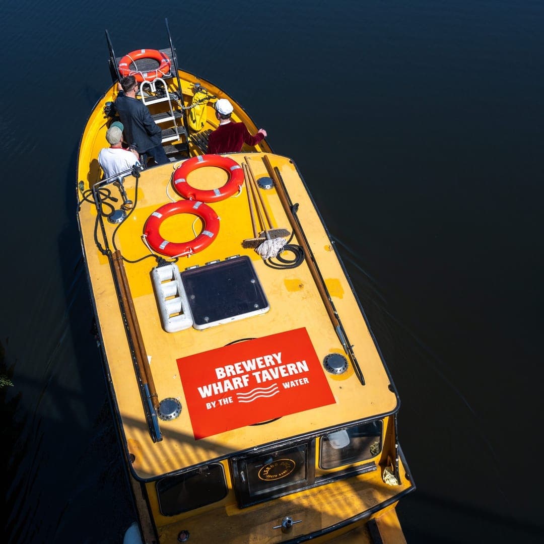 Aerial drone view of a yellow Brewery Wharf Tavern branded boat moored on the water in Leeds