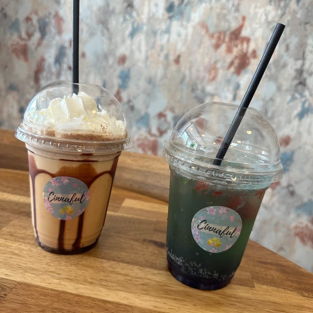 Two Cinnaful branded iced drinks — a chocolate frappe and a matcha — on a wooden café table