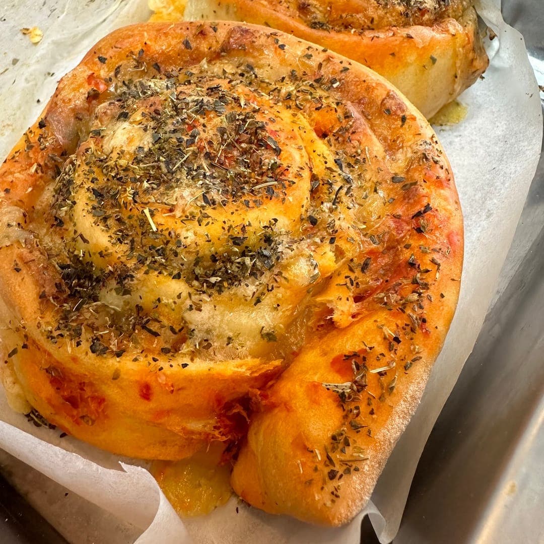 Freshly baked savoury cinnamon rolls with cheese and dried herbs in a baking tray at Cinnaful