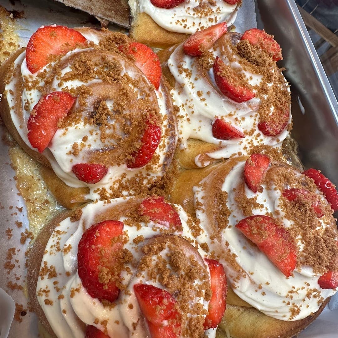 Tray of Cinnaful cinnamon rolls topped with cream, fresh strawberries and brown sugar crumble