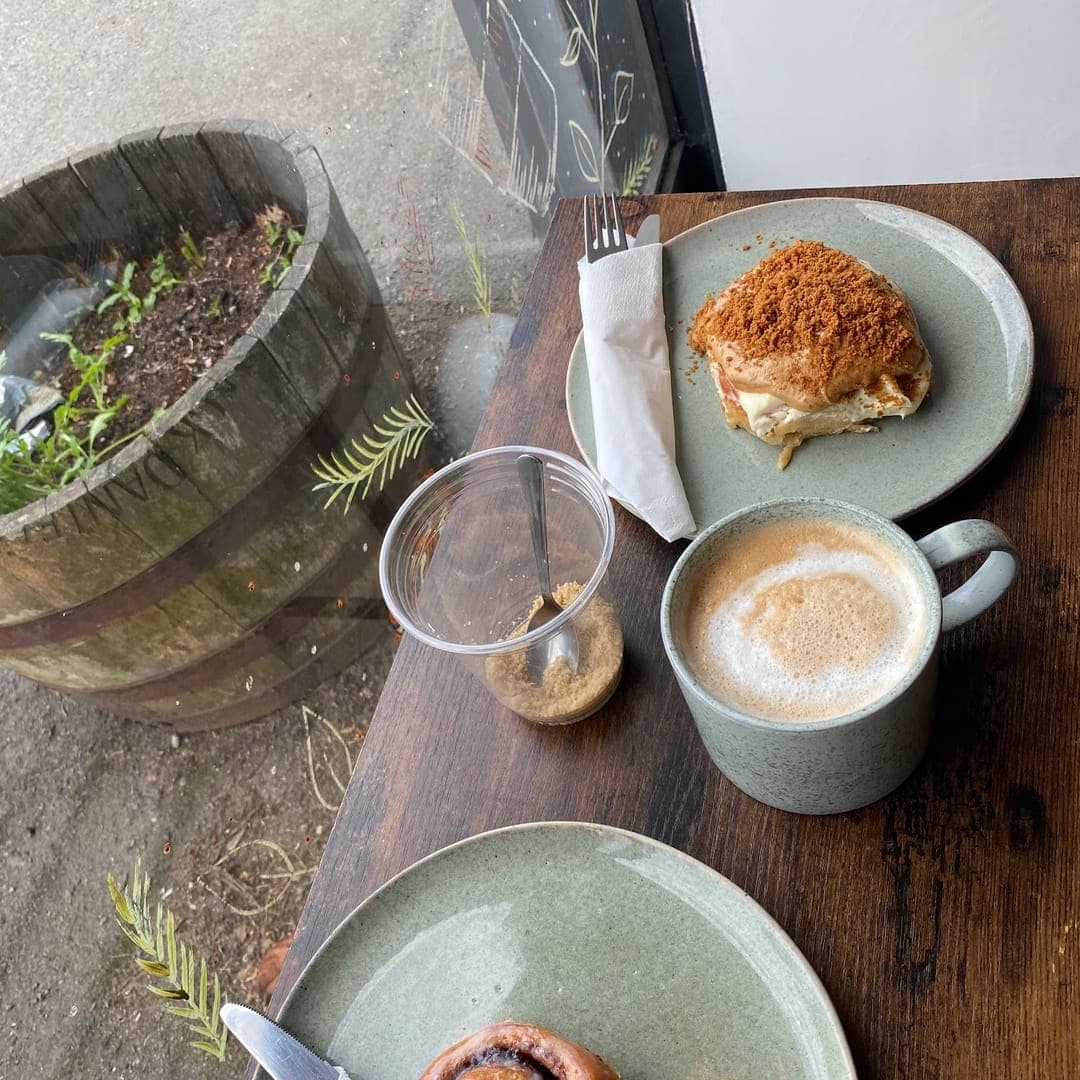 Overhead view of a Cinnaful café table by the window with cinnamon rolls, a latte and a water glass