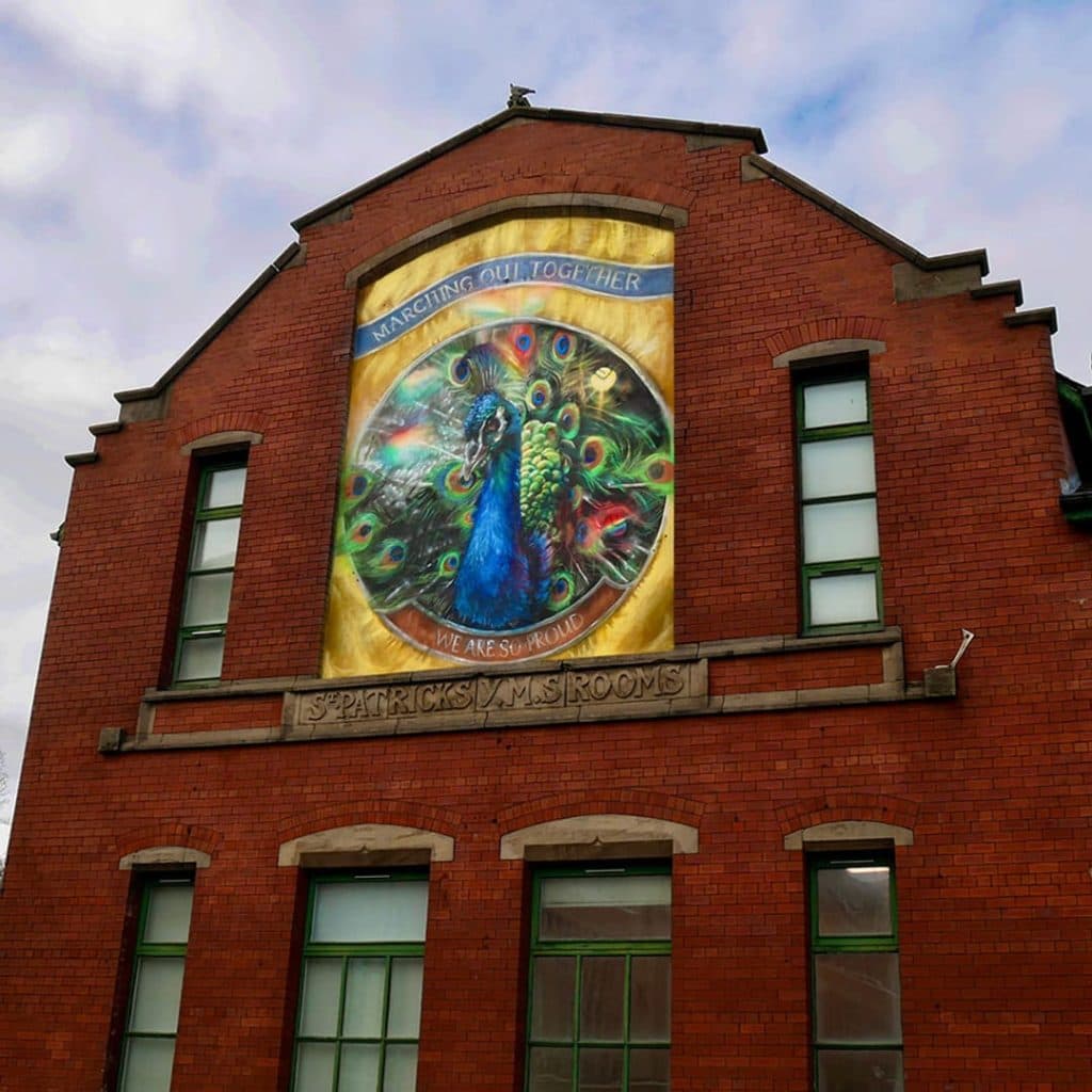Force of Nature mural by Cbloxx on Patrick Studios, Mabgate, Leeds — peacock with "Marching Out Together" banner, an LGBTQ+ tribute reframing the LUFC emblem