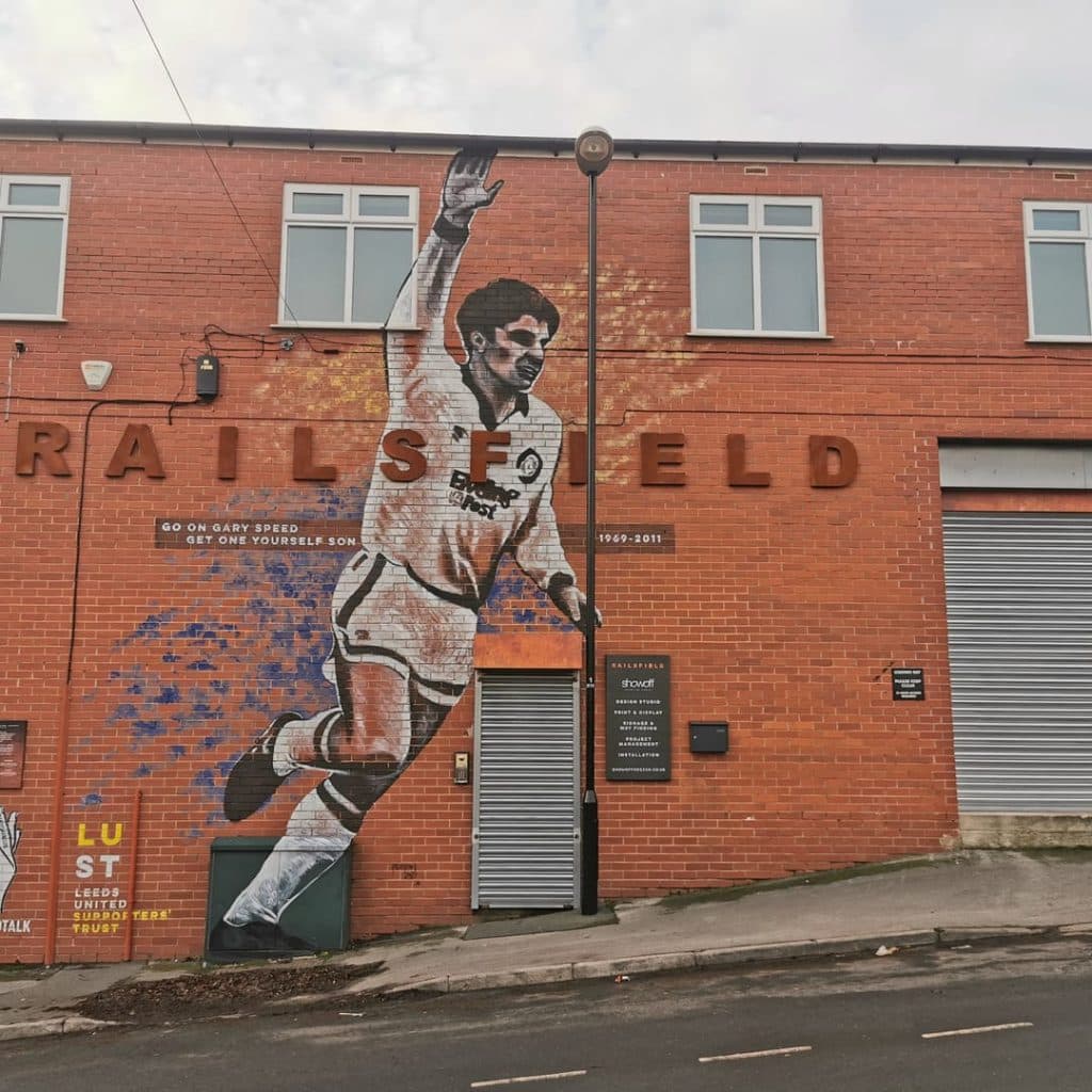 Gary Speed mural by Claire Bentley-Smith (Poshfruit Creative) on ShowOff Design & Display, Stanningley Road, Bramley — Speed celebrating in white kit, with Andy's Man Club logo