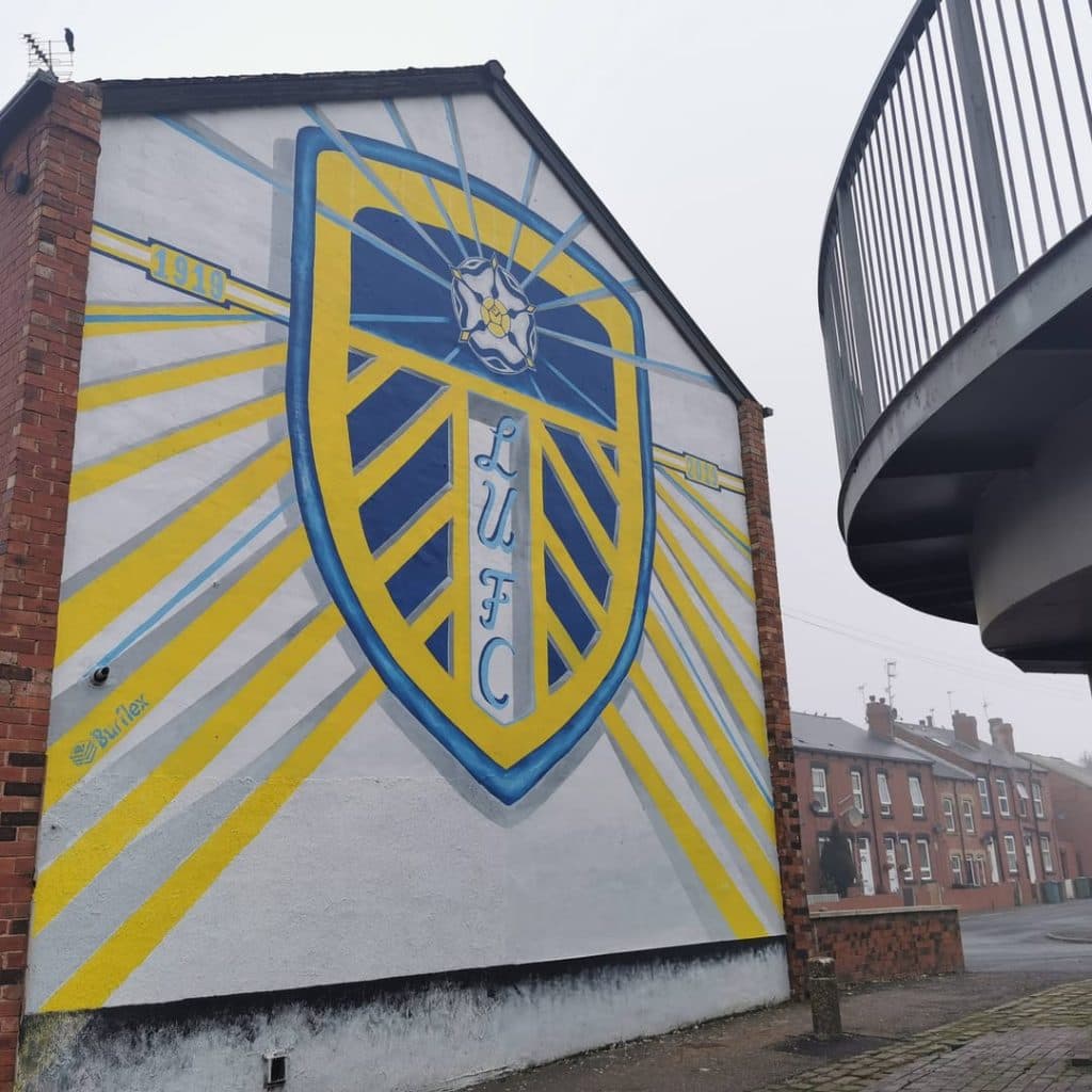 Giant Leeds United centenary badge by Shane Green at 9 Tilbury Mount, Holbeck, Leeds — large LUFC crest spanning two terrace gable ends with 1919-2019 dates
