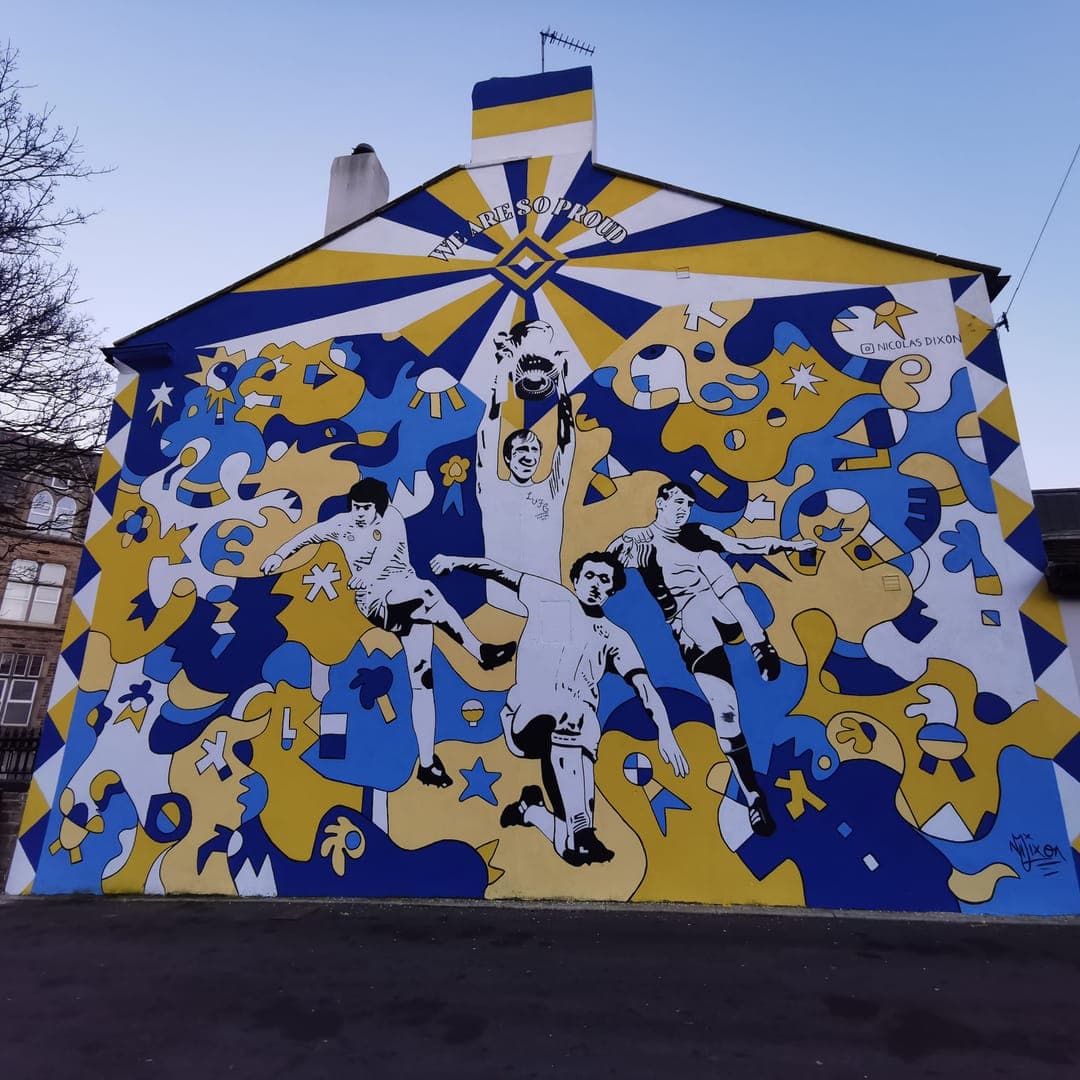 Legends Mural by Nicolas Dixon at Avanta Care, Pudsey Market, Leeds — tribute to Jack Charlton, Norman Hunter, Trevor Cherry and Peter Lorimer in the blue-and-yellow signature pattern