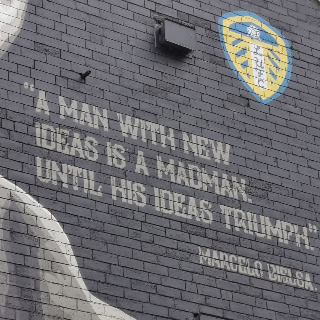 Marcelo Bielsa mural by Tankpetrol on the side gable of One Stop Stores, Hyde Park Road, Leeds — black-and-white portrait with the quote "A man with new ideas is a madman until his ideas triumph"