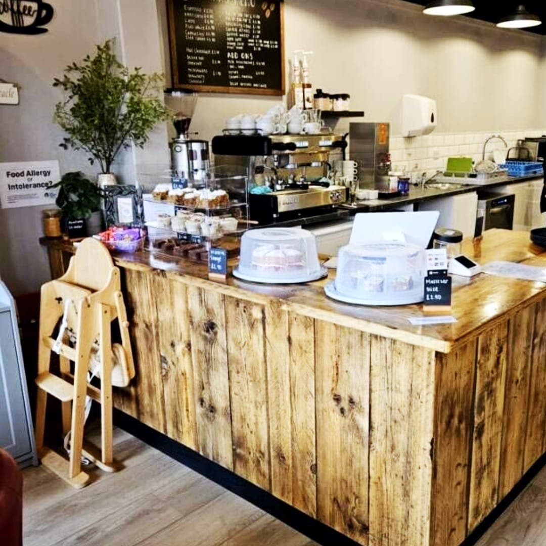 Rustic wooden service counter at Miracle cafe with espresso machine, cake display and indoor plants