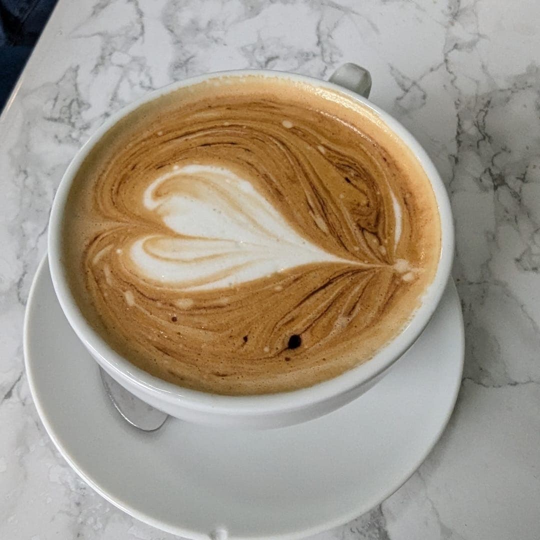 Close-up of a latte with heart-shaped latte art in a white cup on a marble table at Miracle Cafe