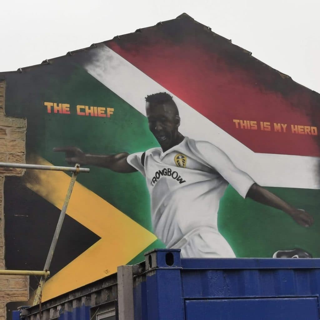 The Chief mural of Lucas Radebe by Adam Duffield at Sweeney Todd Barbers, Potternewton Lane, Leeds — Radebe in white Strongbow Leeds kit on a South African flag background
