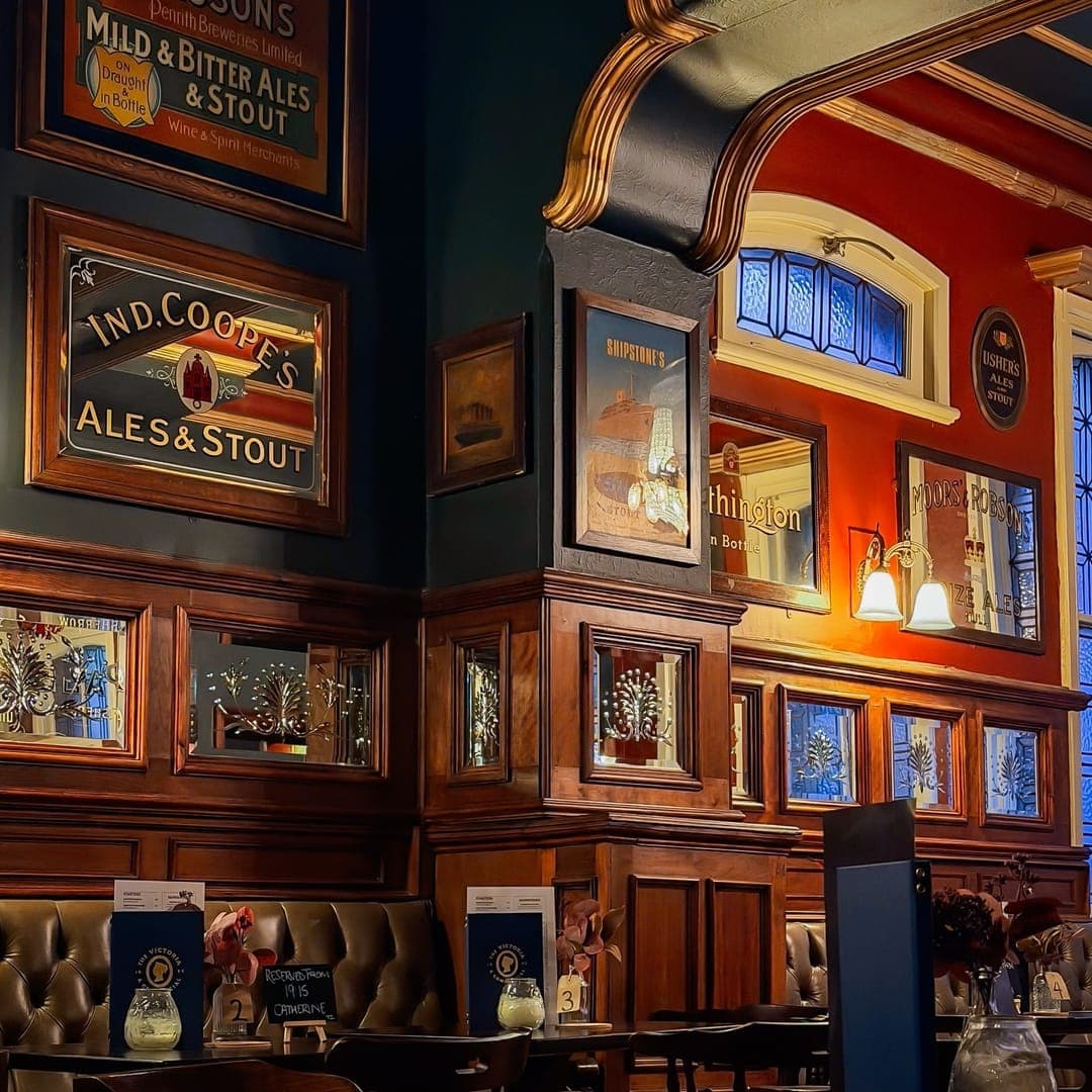 Wood-panelled Victorian pub interior at The Victoria and Commercial with vintage brewery advertising signs and leather booth seating