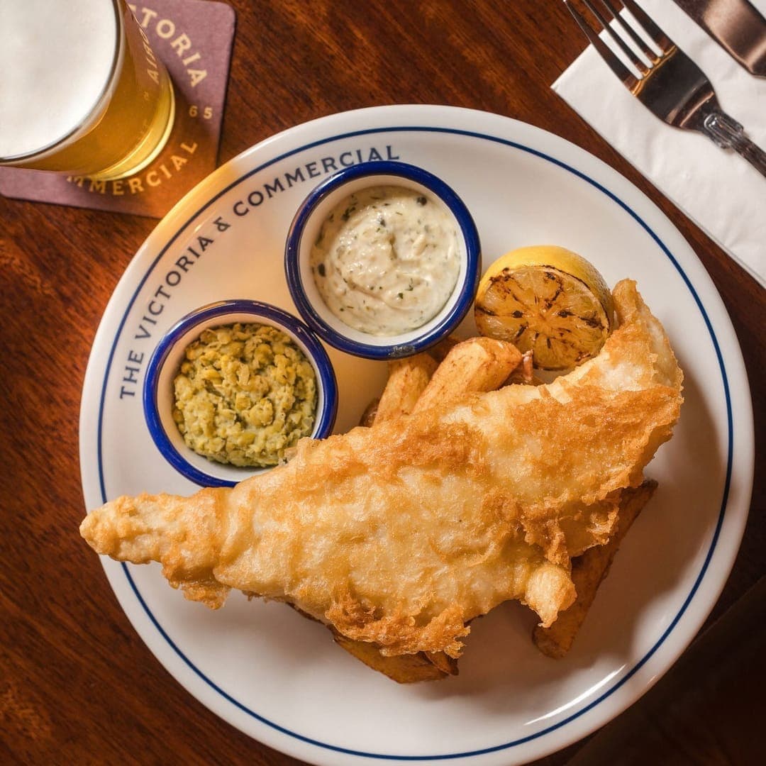 Golden beer-battered fish with mushy peas, tartare sauce and lemon on a branded Victoria and Commercial plate