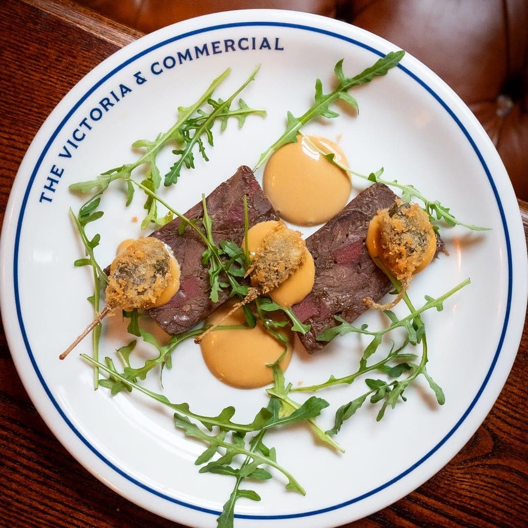 Sliced ox tongue and cheek terrine with rocket salad and sauce dots on a branded Victoria and Commercial plate
