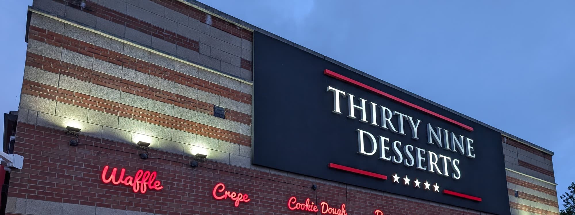 The shopfront signage of 39 Desserts at Cardigan Fields Leisure Park, Leeds, with a large THIRTY NINE DESSERTS sign on a black fascia and red script menu words for Waffle, Crepe, and Cookie Dough below.
