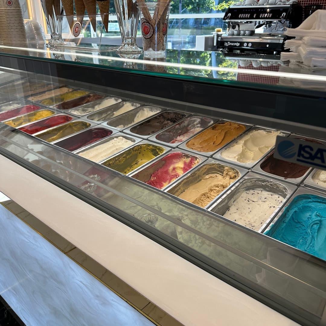 A long gelato counter at 39 Desserts, Leeds, displaying rows of brightly coloured gelato tubs in flavours such as raspberry, pistachio, chocolate, peanut butter, vanilla and bubblegum, with cone holders on top.