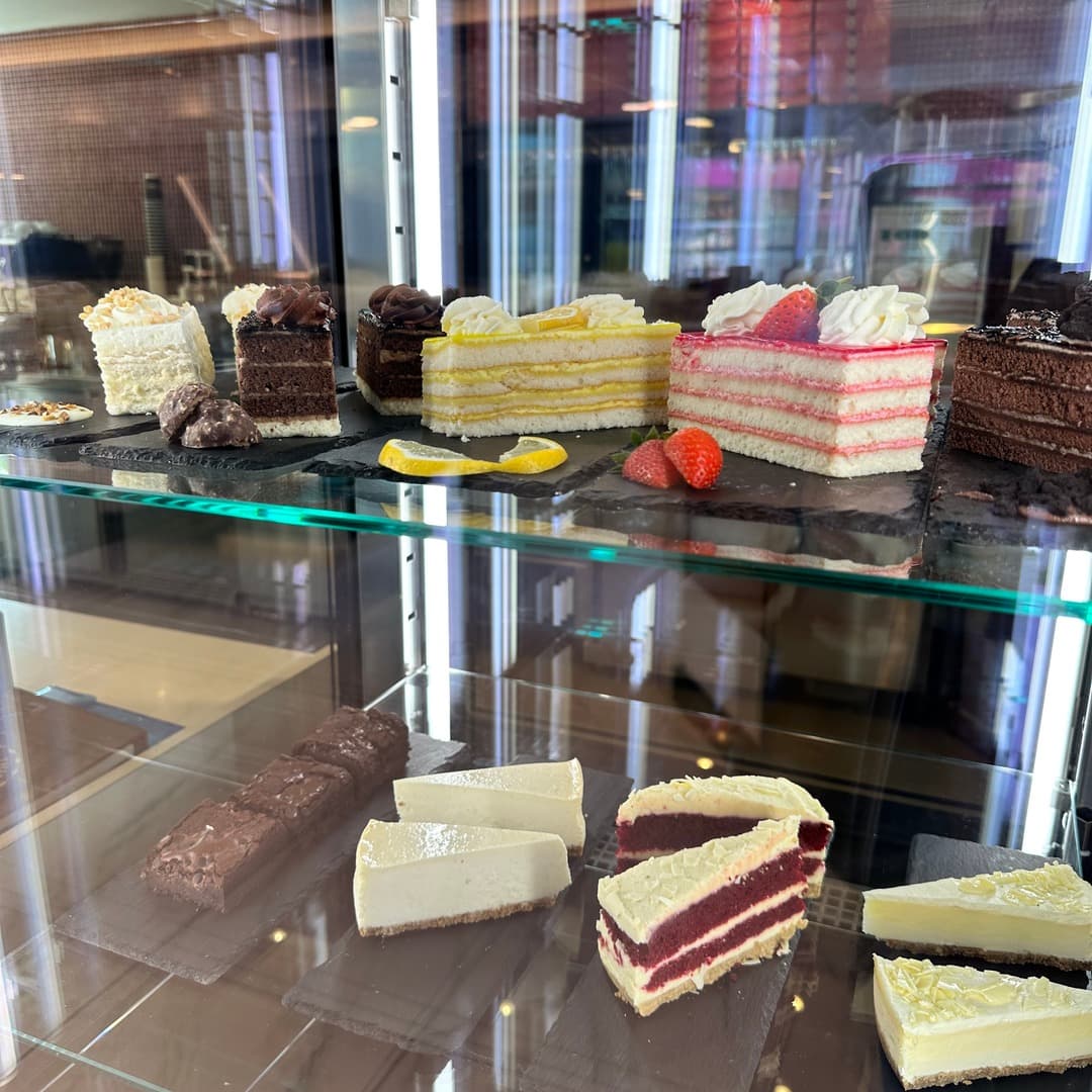 A glass display case at 39 Desserts, Leeds, with slices of chocolate cake, lemon mille-feuille, raspberry layered cake, red velvet cake, and a vanilla cheesecake.