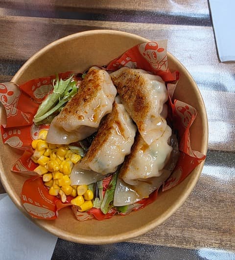 Pan-fried handmade gyoza with corn and lettuce in a branded paper bowl at Amazing Gyoza, Kirkgate Market, Leeds.