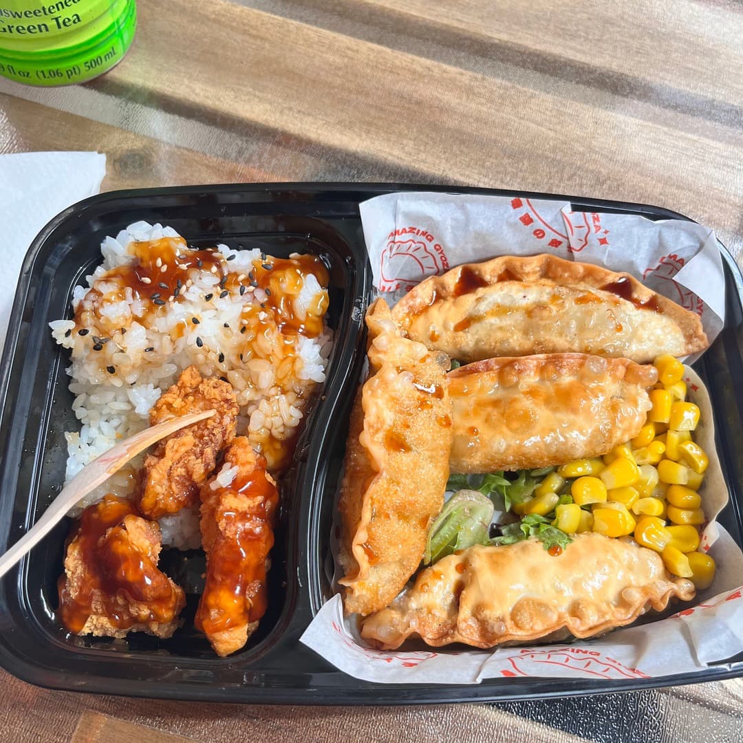 A bento box from Amazing Gyoza, Leeds, with glazed chicken on rice, fried gyoza, sweetcorn and lettuce, served with a bottle of green tea.