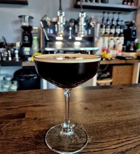 An espresso martini in a coupe glass at Ankave Coffee and Cocktails, Leeds, with the espresso machine and bottle shelves in the background.